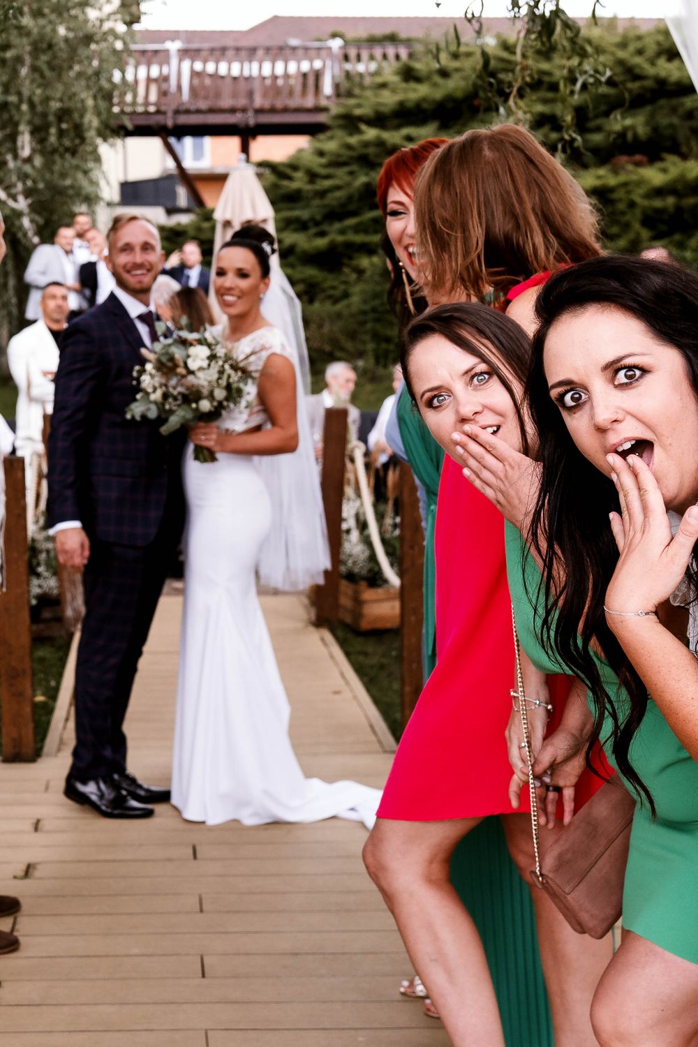 Wedding party members react playfully in foreground while couple poses on deck.