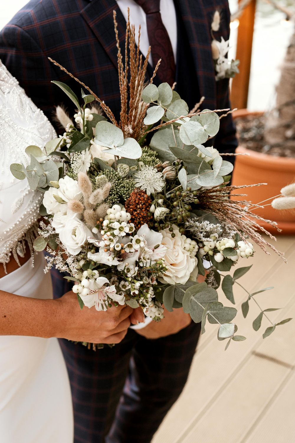A rustic wedding bouquet with white roses, eucalyptus leaves, and dried grasses in a natural boho style.