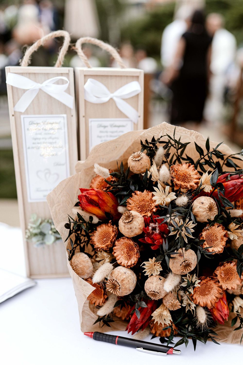 Rustic wedding favors in kraft paper bags with white bows alongside a beautiful bouquet of peach and red flowers.