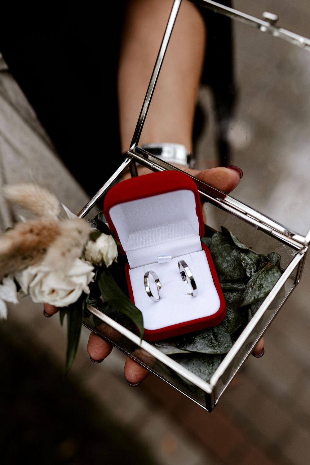Silver engagement ring box with two wedding bands displayed on a mirrored surface.
