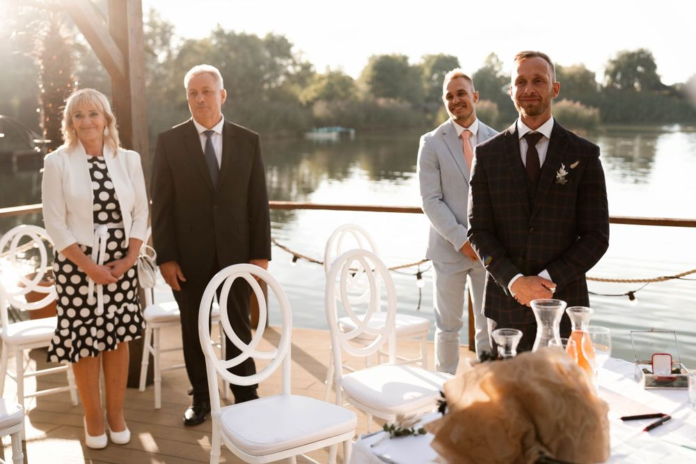 An intimate waterfront wedding reception setup with white chairs and table settings at sunset.