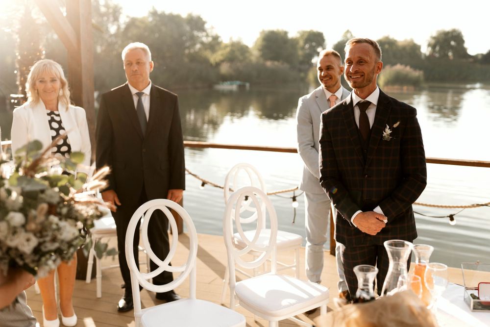 Wedding ceremony setup by the water with white chairs and floral arrangements in golden sunlight.