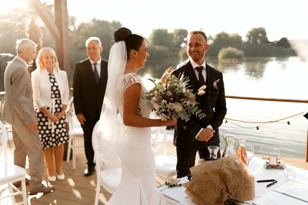 A waterfront wedding ceremony with bride holding a lush bouquet of mixed flowers.
