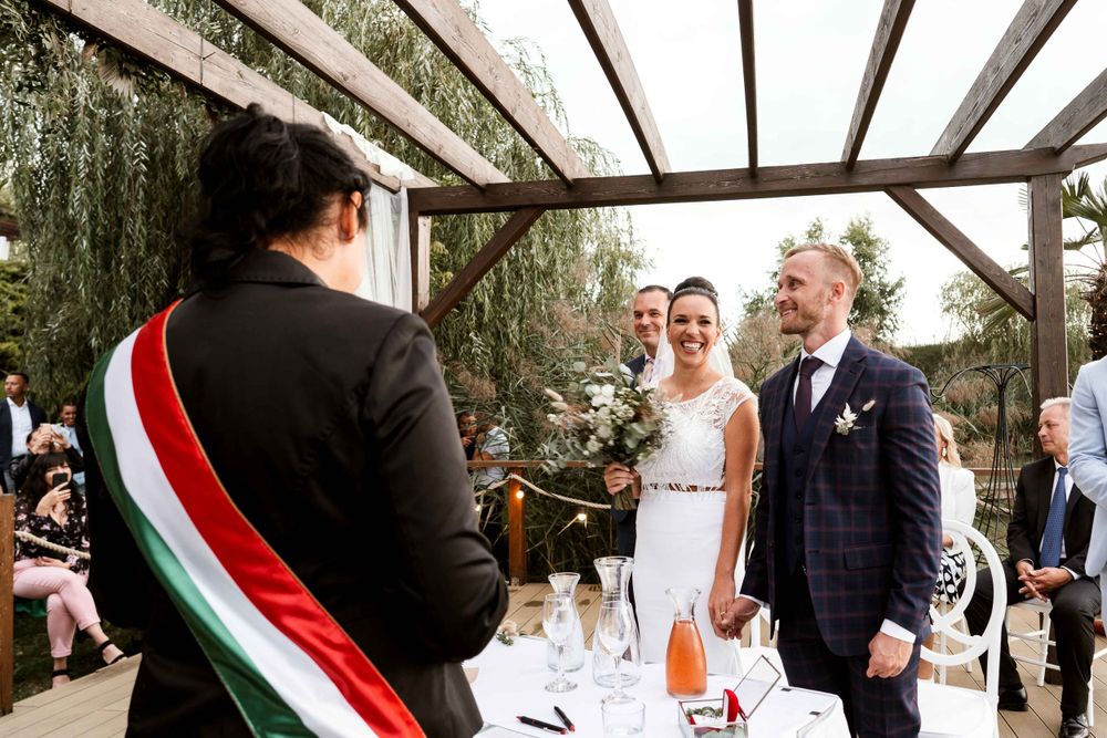 Outdoor wedding ceremony under wooden pergola with official wearing Italian flag sash.