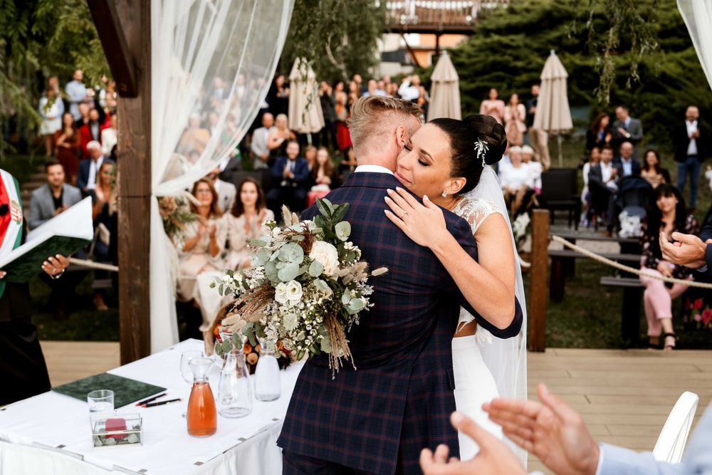 Emotional embrace during outdoor wedding ceremony under decorated pergola.