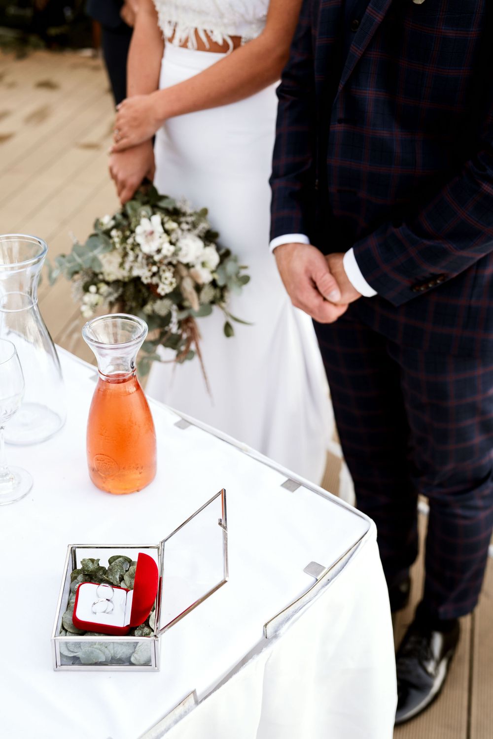 Wedding couple standing by table with orange drink carafe and decorative box.