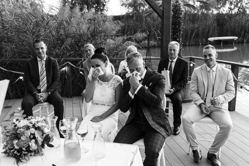 Black and white photo of wedding guests and newlyweds enjoying reception on an outdoor deck.