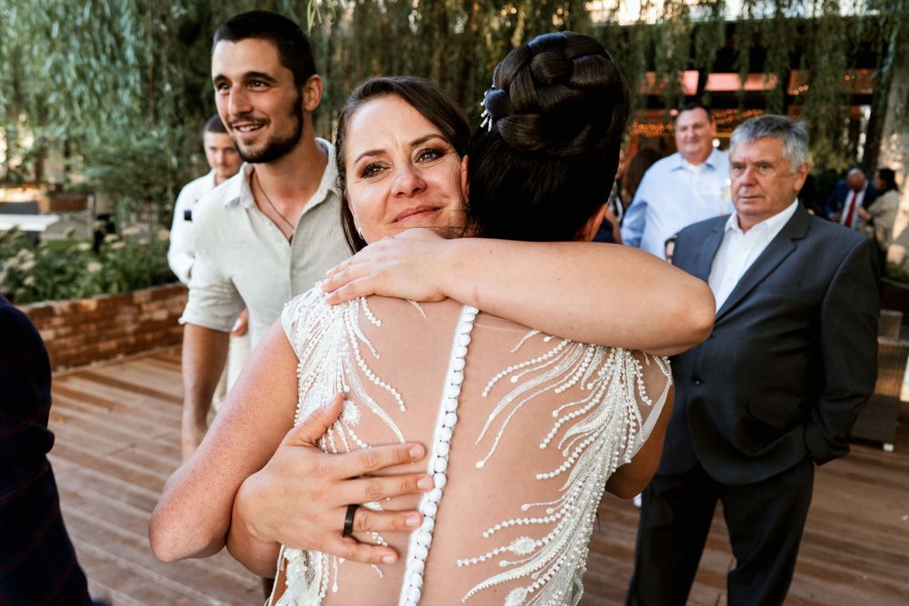 Guests share emotional embraces during a wedding reception on an outdoor patio.