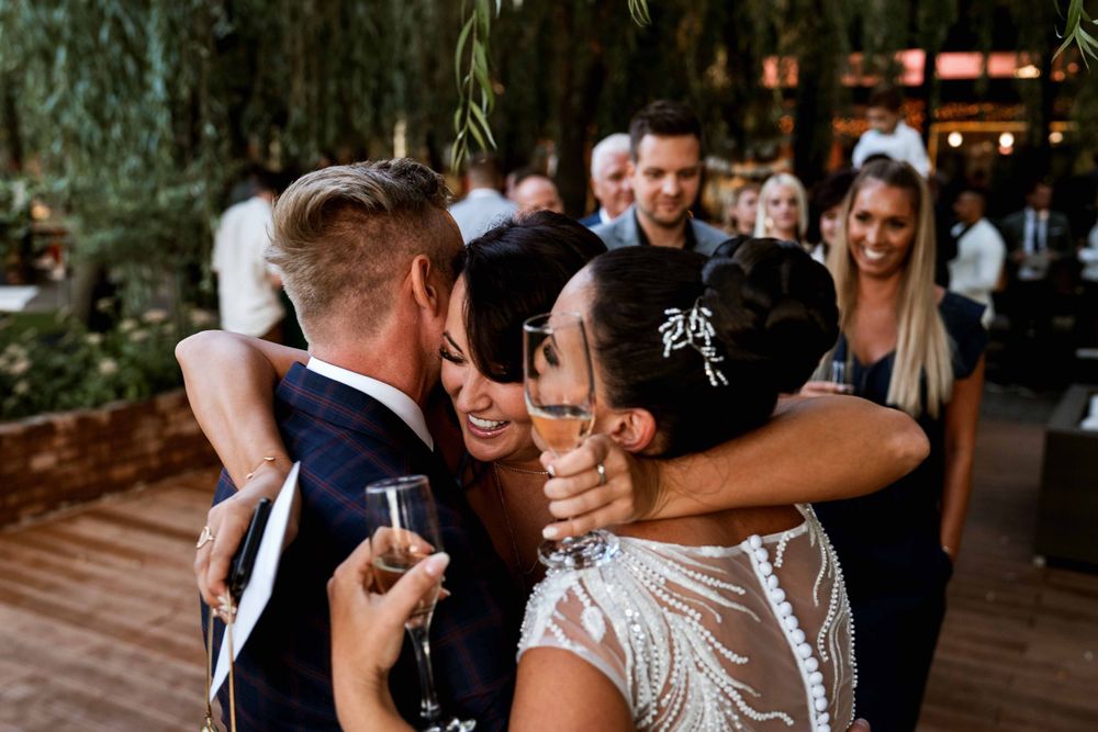 Guests celebrate with drinks and embraces at an outdoor wedding reception.