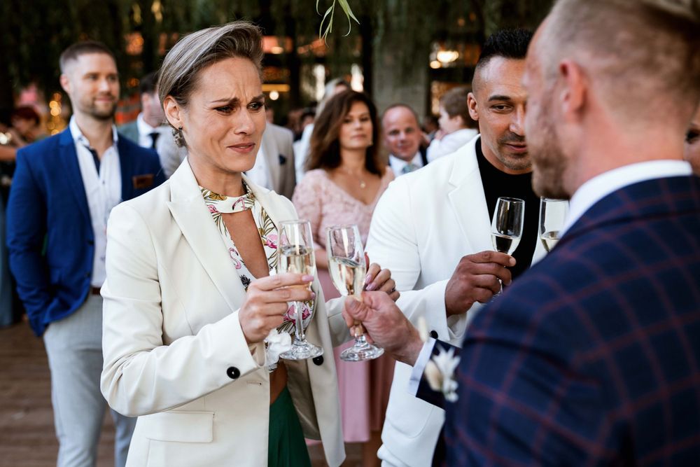 Guests in formal attire toast with champagne glasses at outdoor wedding reception.