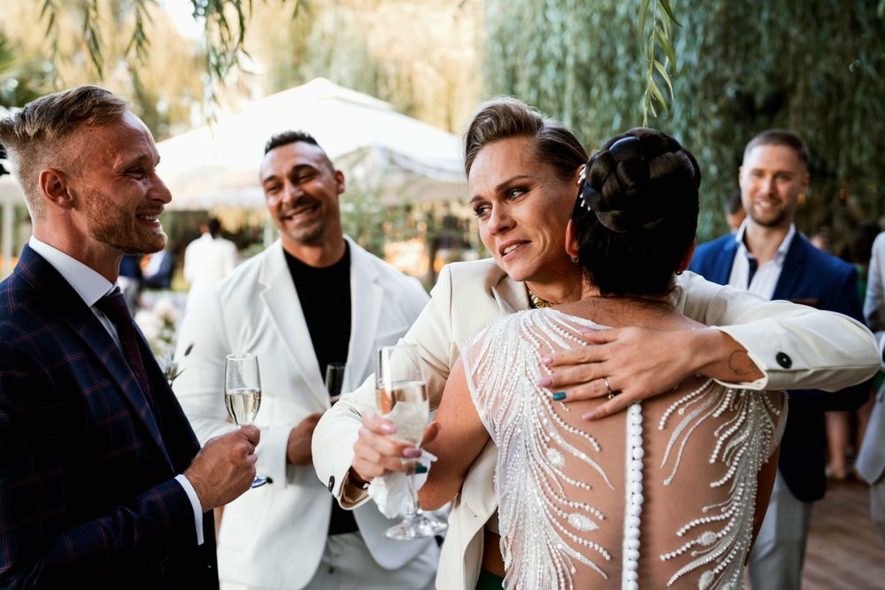 Wedding celebration on outdoor patio with guests sharing drinks and hugs.