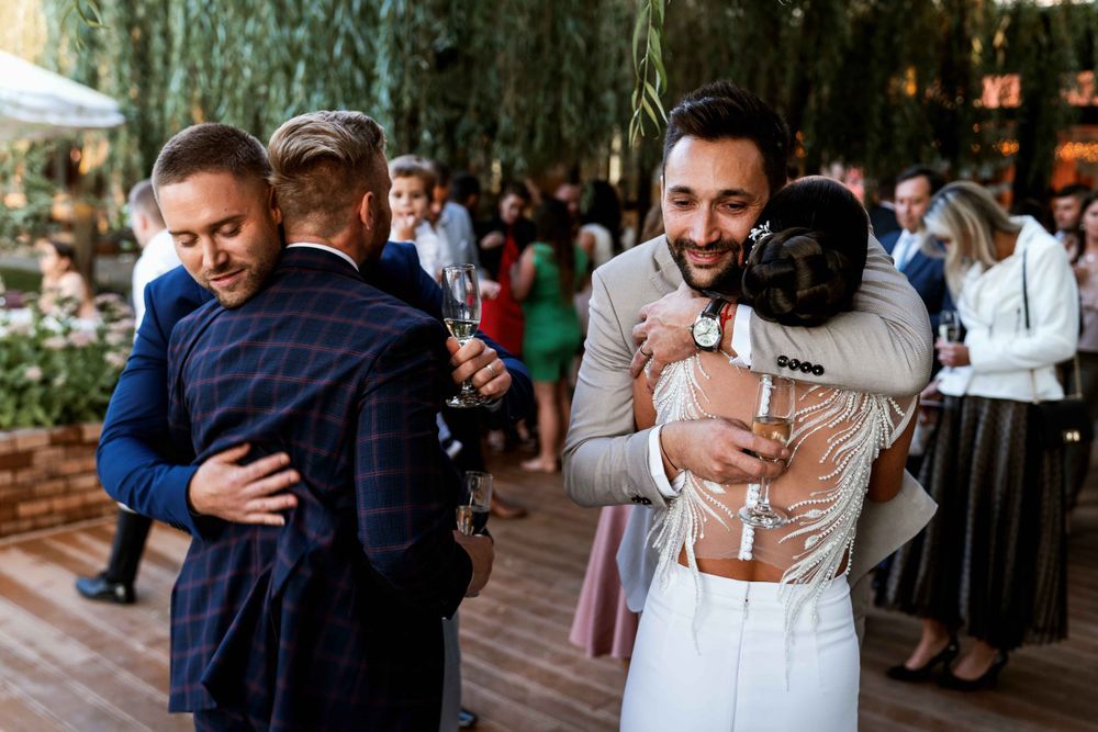 Two emotional embraces being shared during what appears to be a wedding reception on an outdoor deck.