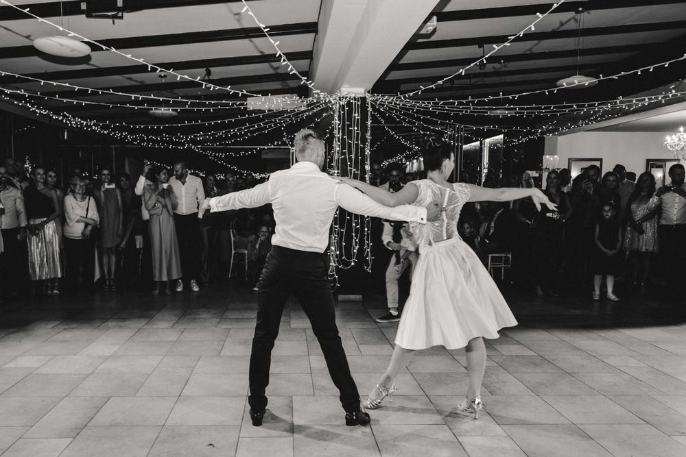 A couple performs an energetic dance move on a reception floor decorated with string lights.