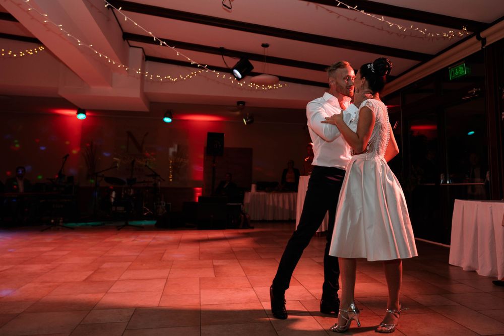 A couple dancing in an intimate moment under dramatic red lighting at a reception venue.