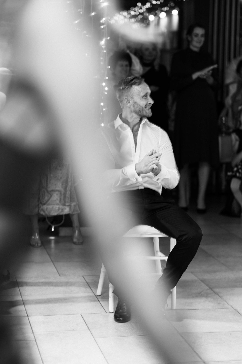 Black and white photo of someone sitting on a chair under string lights at an event.