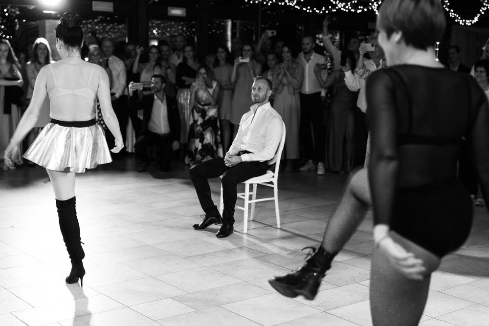 Black and white image of dancers performing at a reception with guests watching in background.