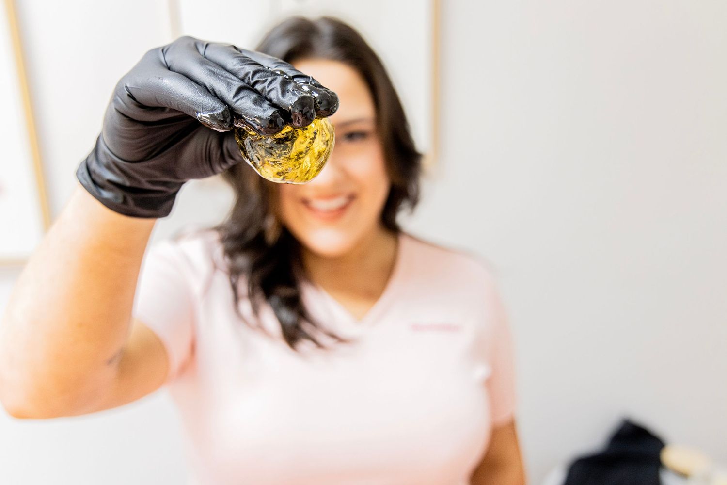 Hand in black glove holding up clear liquid in medical setting.