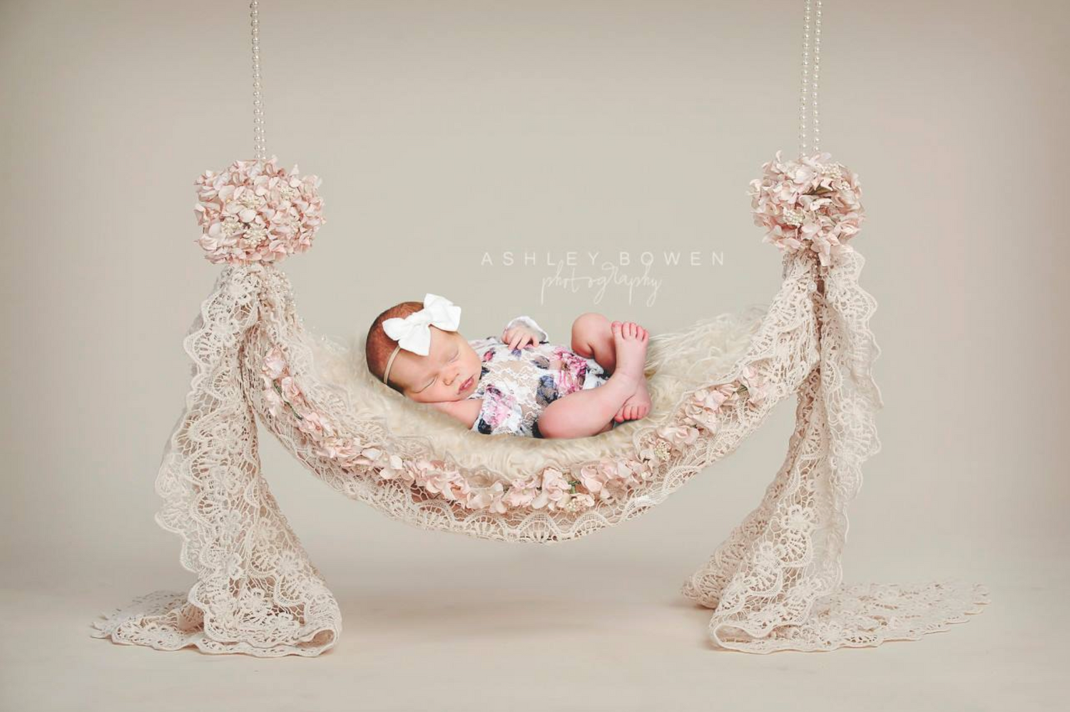 Newborn baby girl sleeping peacefully in a lace hammock with floral decorations.