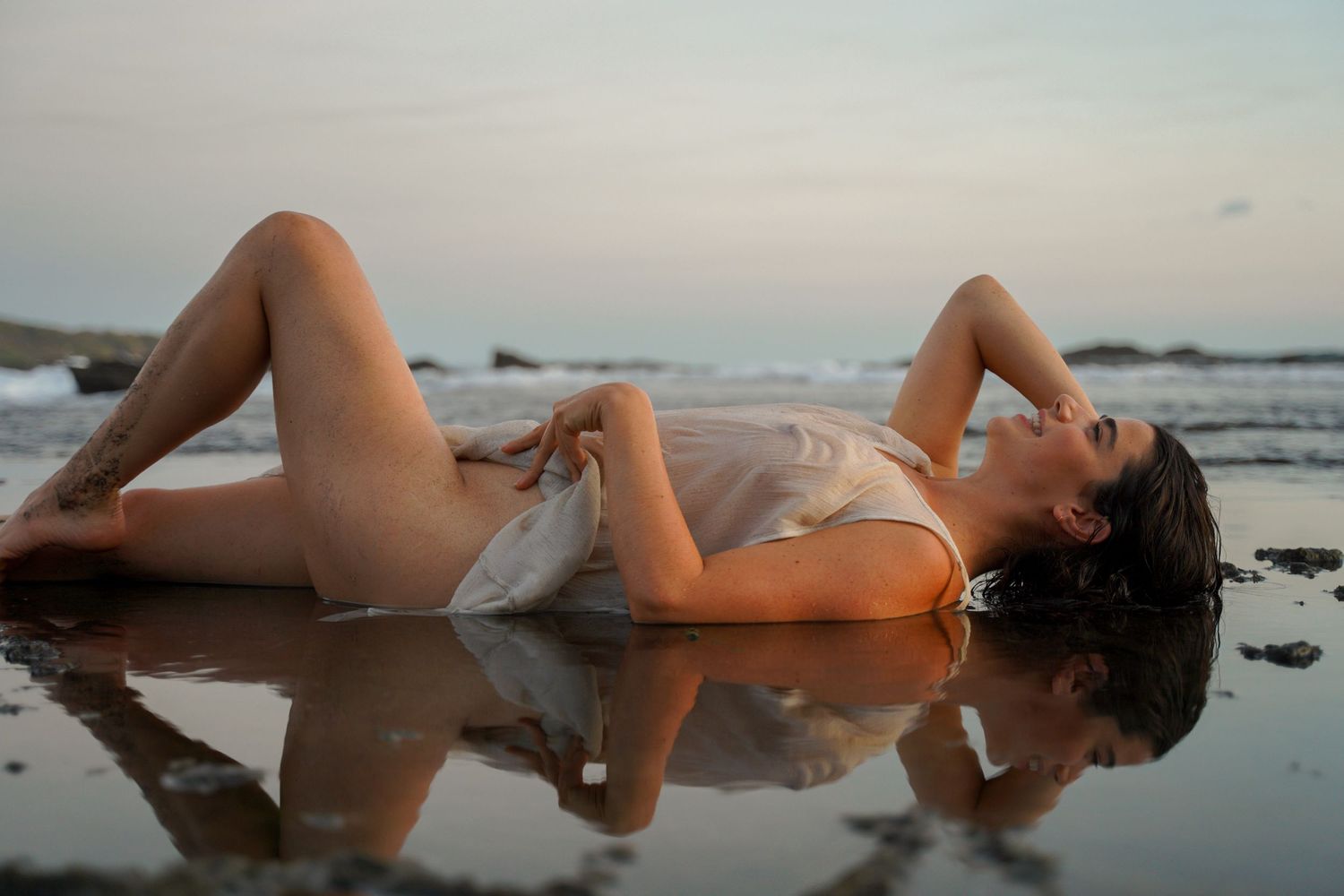 Artistic beach photography with reflections in tidal pools at sunset.