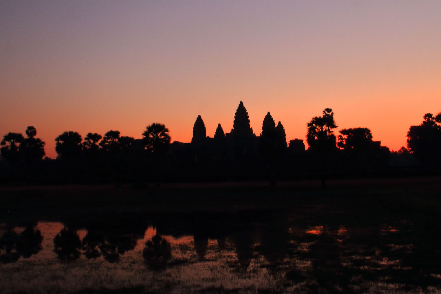Dark silhouettes of Angkor Wat towers against pink and purple dawn sky.