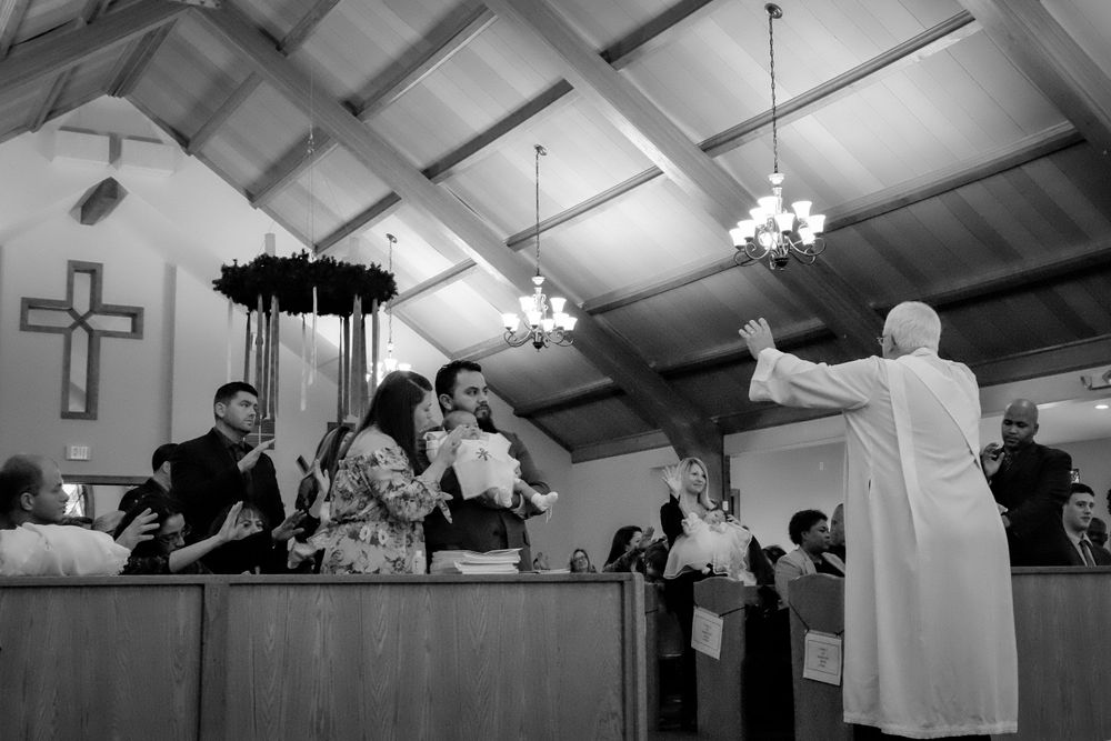 Black and white photo of religious ceremony in church with cross visible on wall.