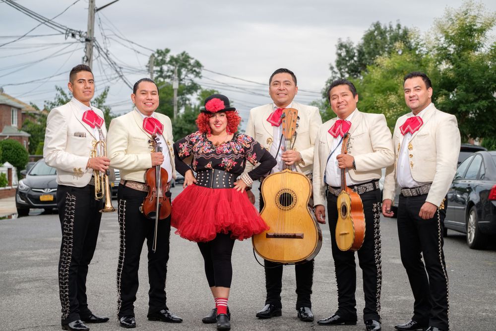 Mariachi band in white suits posing with instruments outdoors.