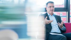 Business professional in glasses sits on public transit while looking at smartphone during commute.