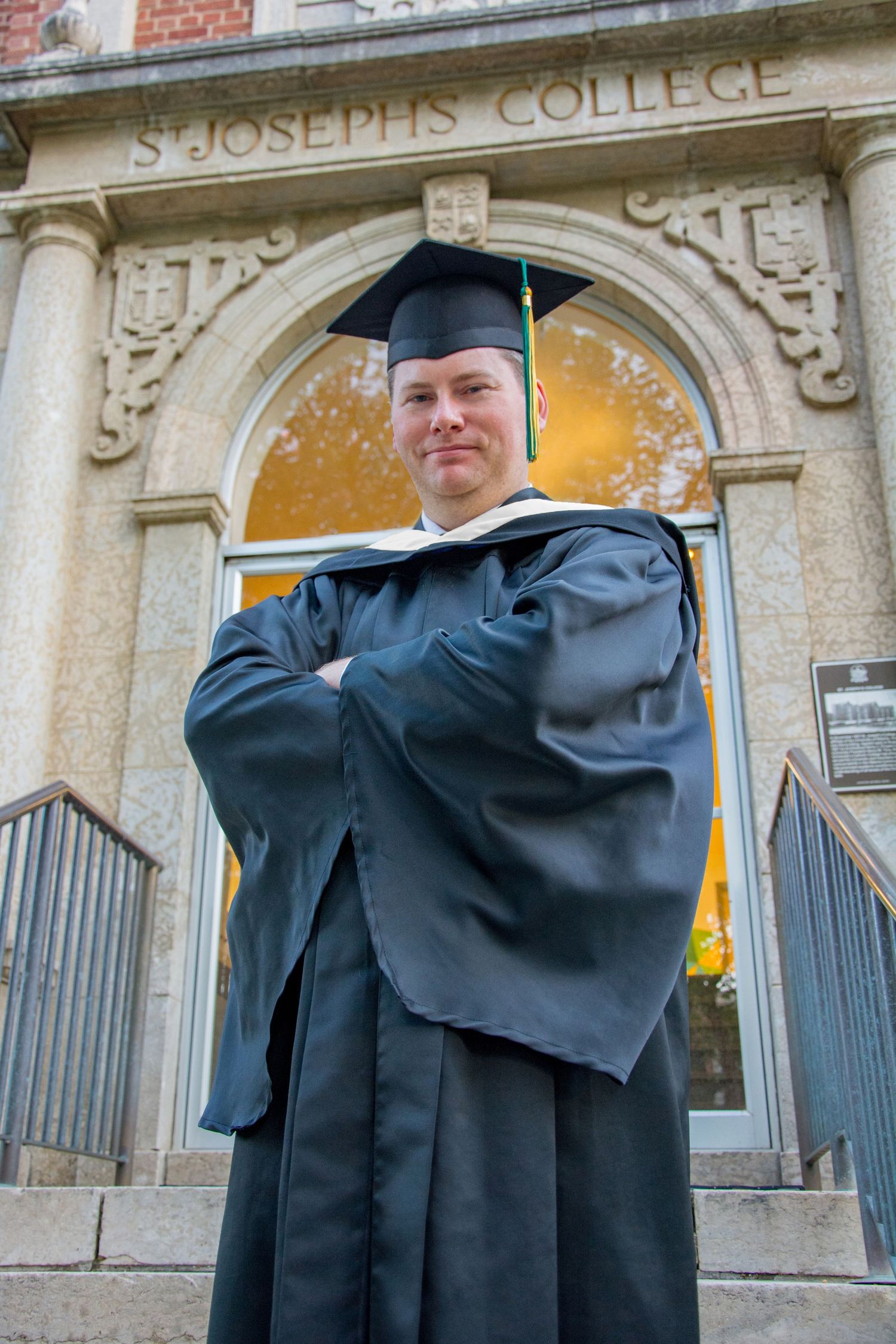 graduate stands in front of old building at the u of a in edmonton in full graduation gown and cap