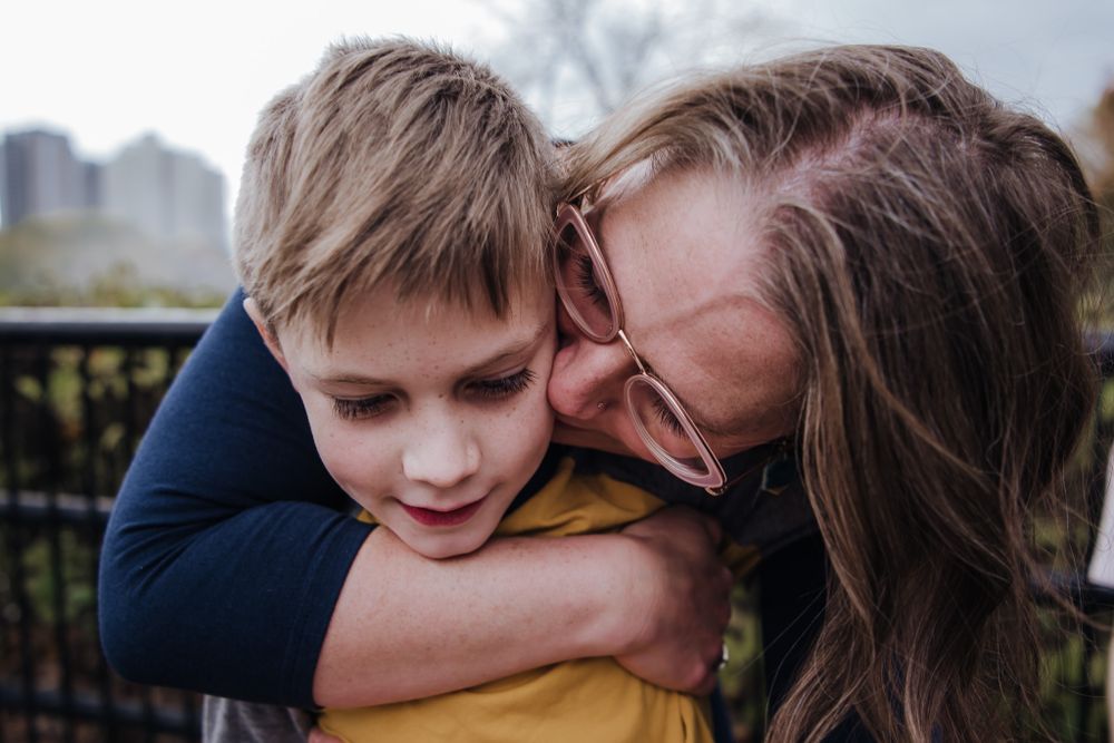 Colour photo of a Caucasian woman holding her young son and giving him a kiss on his cheek.
