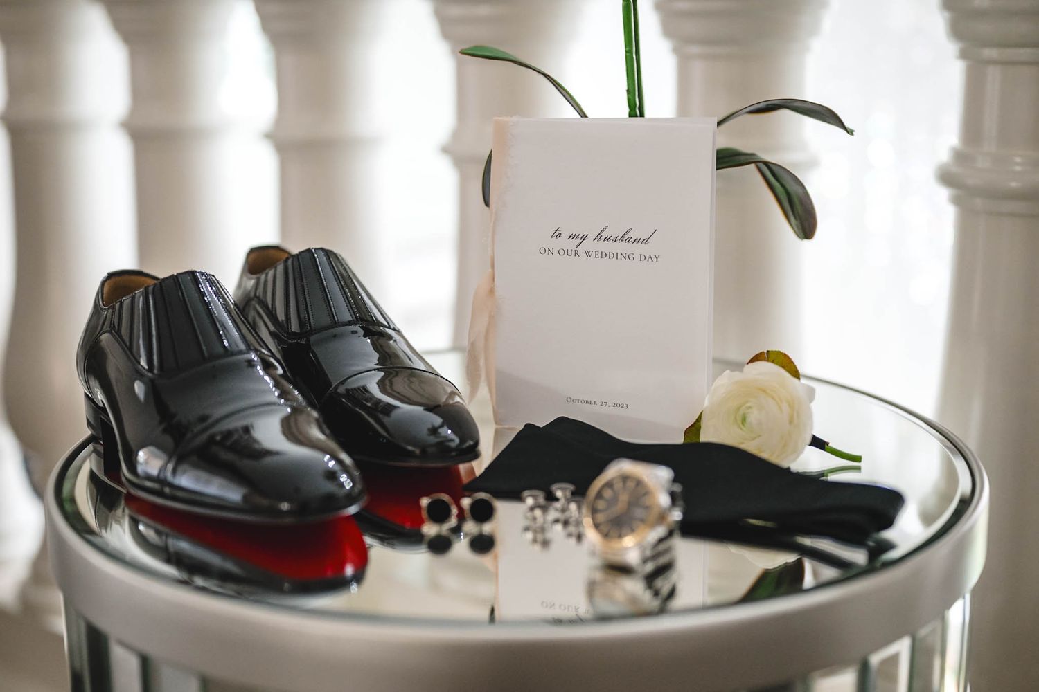 Groom's accessories and formal shoes arranged on white table with classical decor.