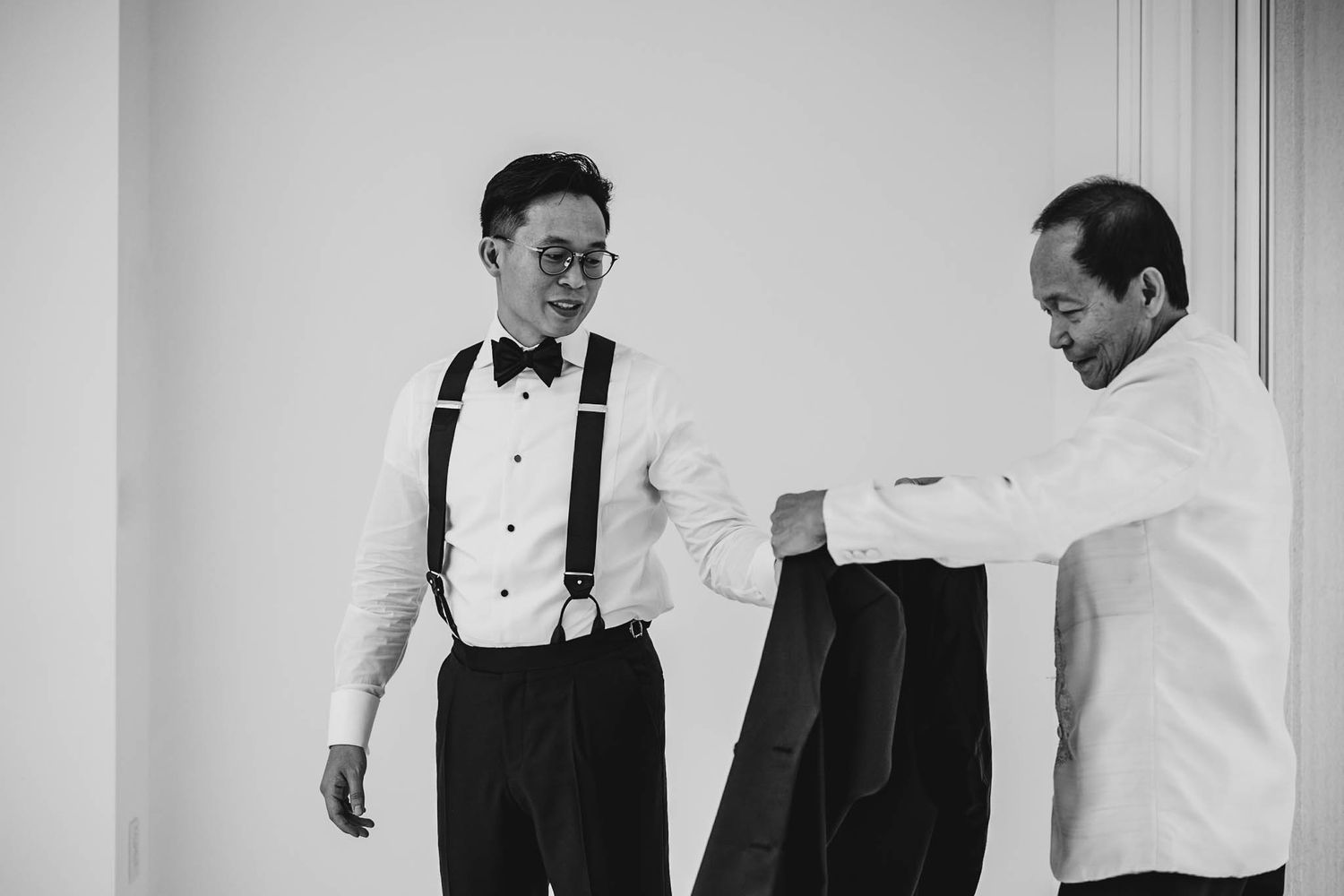 Two men in formal wear assist with wedding preparations in a black and white photo.