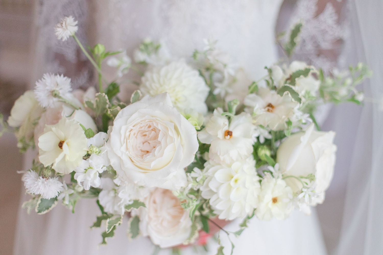 Elegant white and blush floral arrangements with roses and greenery displayed at a wedding.