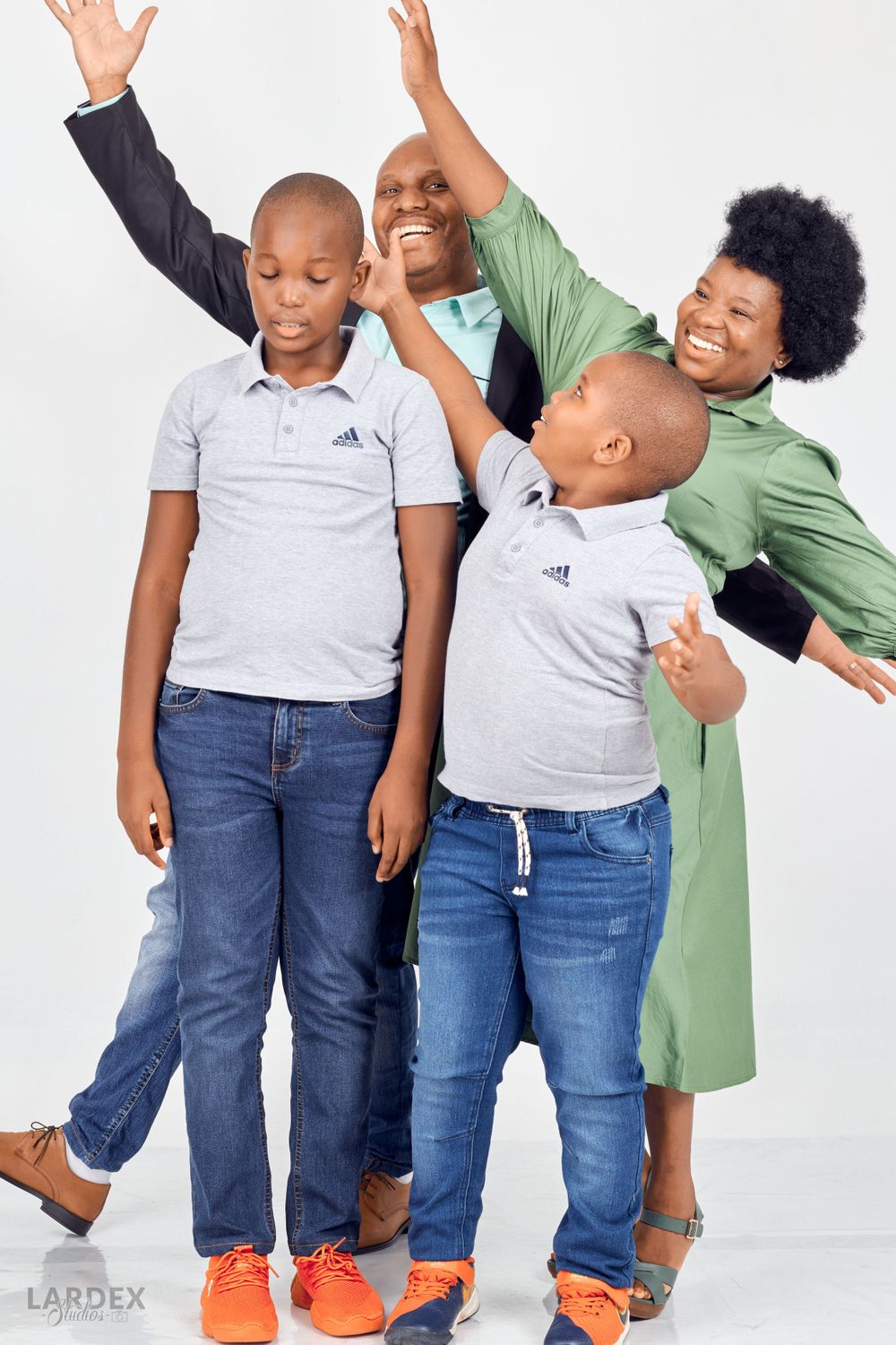 Playful family photo with members making energetic poses against white backdrop.
