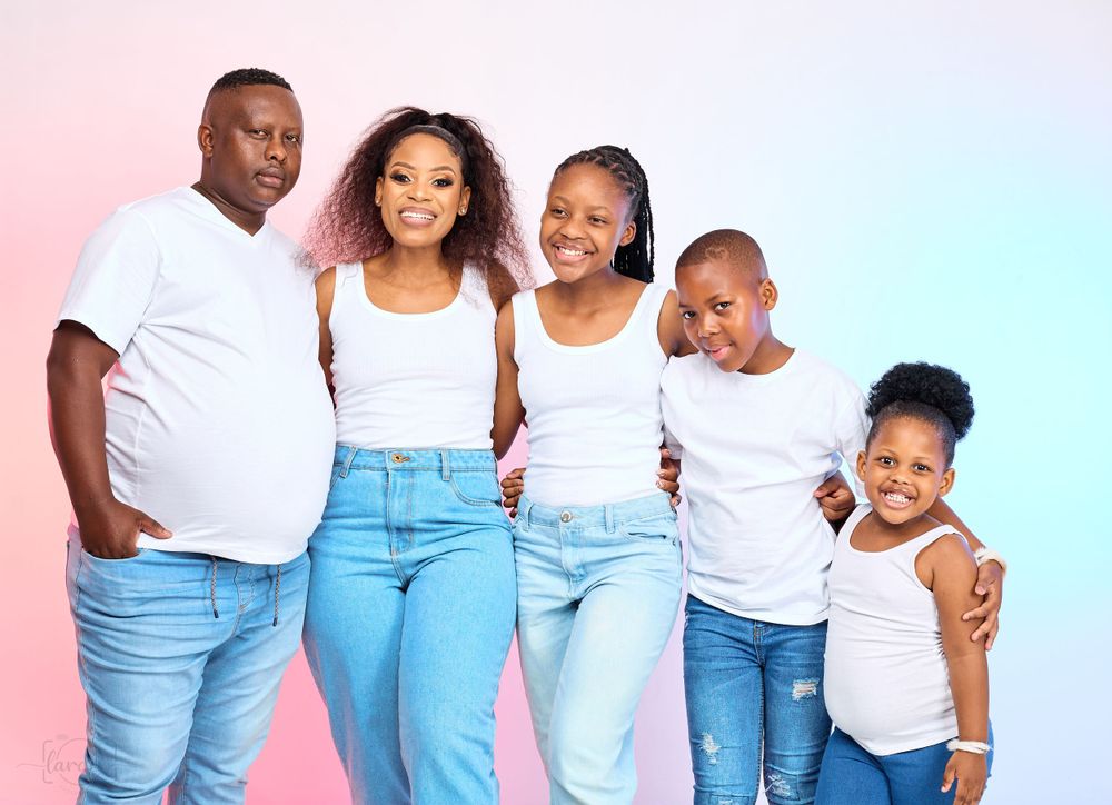 Family of five in coordinated white tops and blue jeans posing against a gradient background.