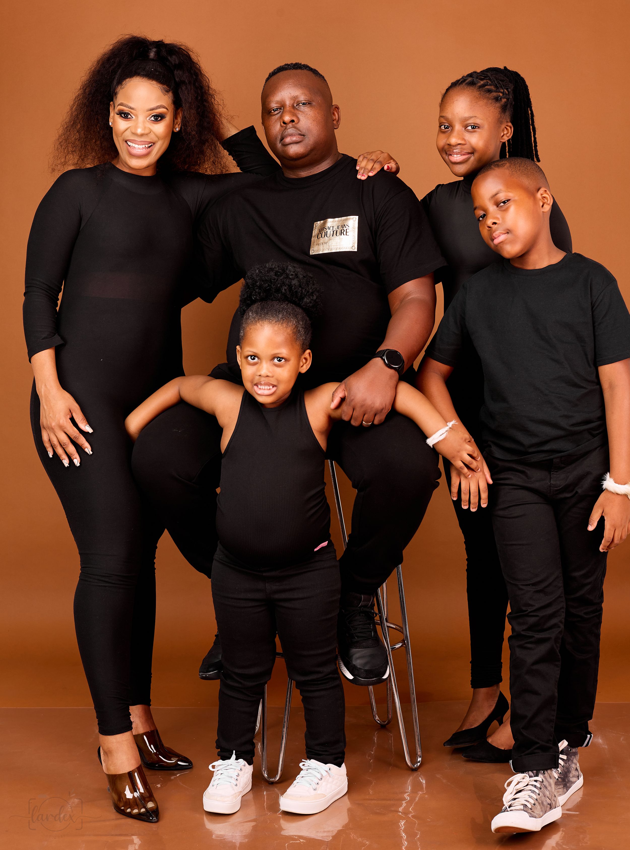 Family of five wearing matching black outfits posing against an orange background for a studio portrait.