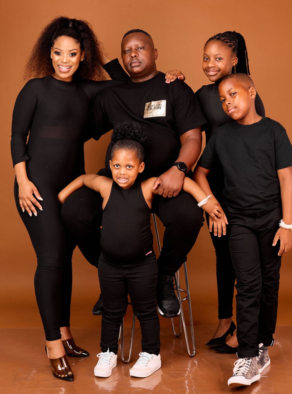Family of five wearing matching black outfits posing against an orange background for a studio portrait.