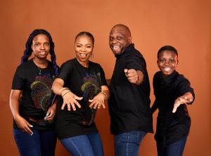 Family wearing matching black tops with gold designs posing against orange background.