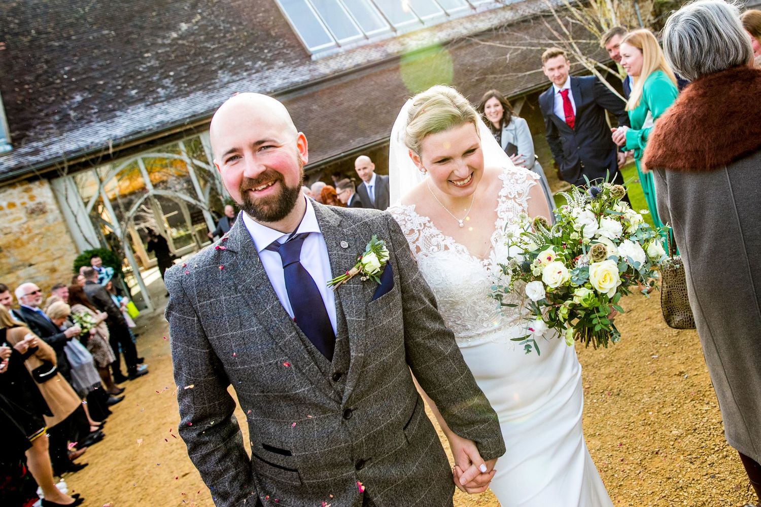 Joyful newlyweds walking through crowd on grounds of rustic venue.