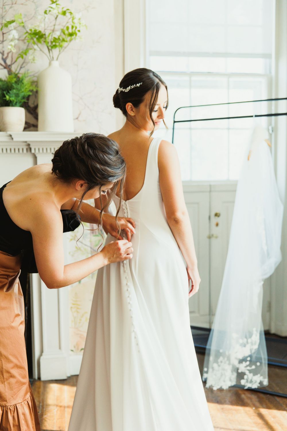 Behind the scenes moment of wedding dress preparations in a bright sunlit room.