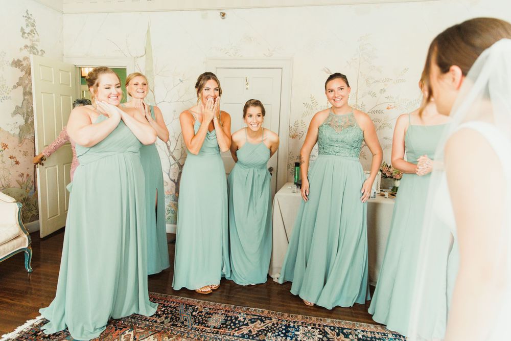 Bridesmaids in matching mint green dresses standing together in an elegant room.