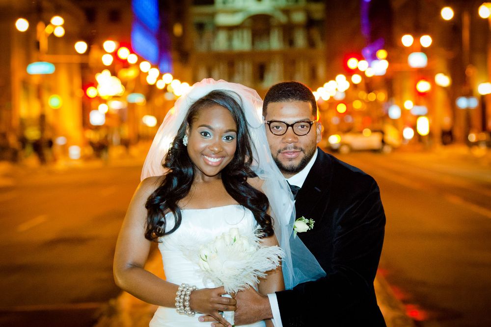 Elegant wedding portrait at night with glowing city lights creating a romantic urban backdrop.