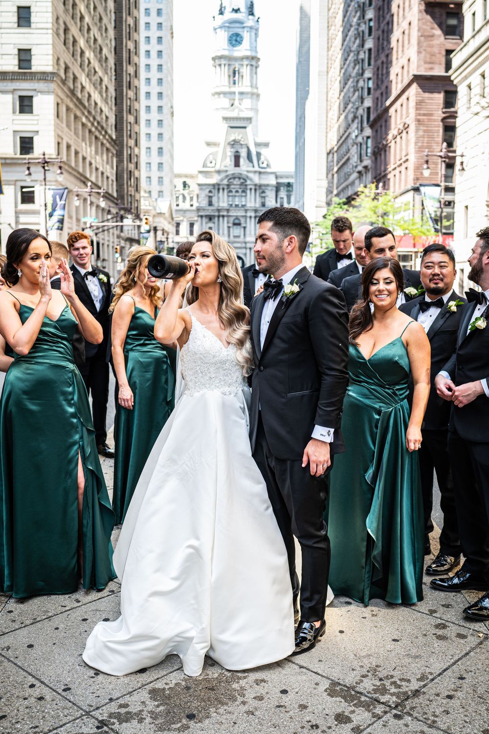 A wedding party poses on a Philadelphia street with bridesmaids in emerald green dresses.