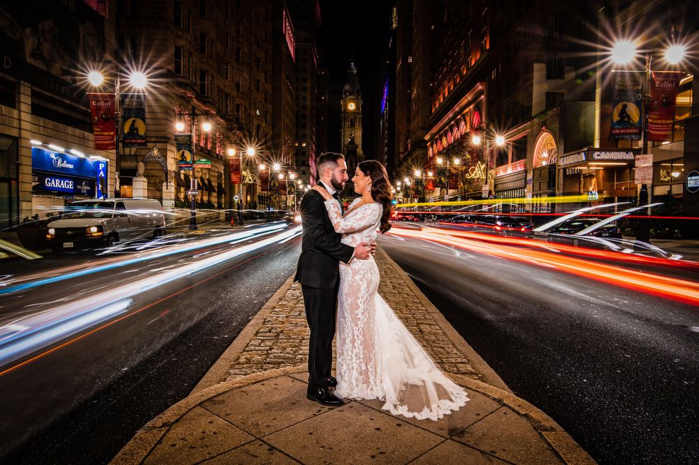 Couple in formal attire sharing romantic moment at night on city street with light trails from passing cars.