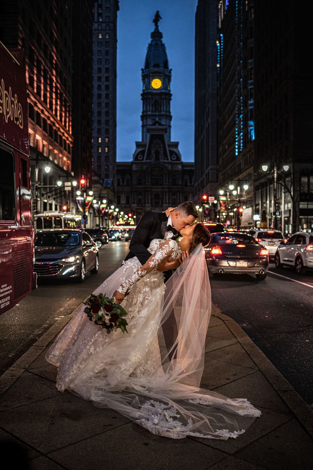 A dramatic wedding photo with a flowing veil against the backdrop of Philadelphia's lit-up Broad Street at night.