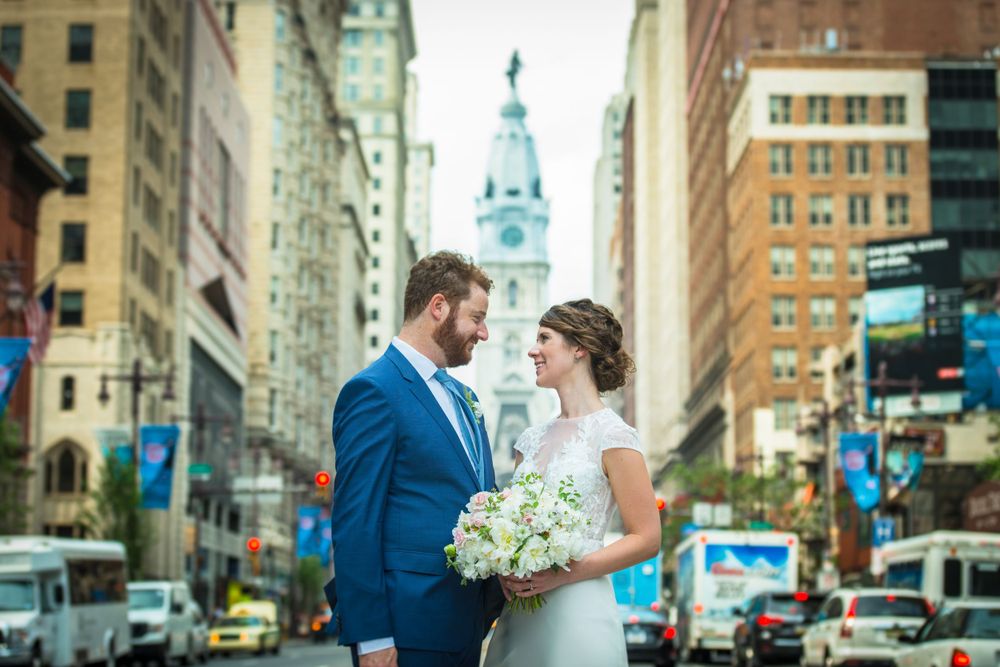 A wedding couple poses on a Philadelphia city street with historic architecture and City Hall in the background.