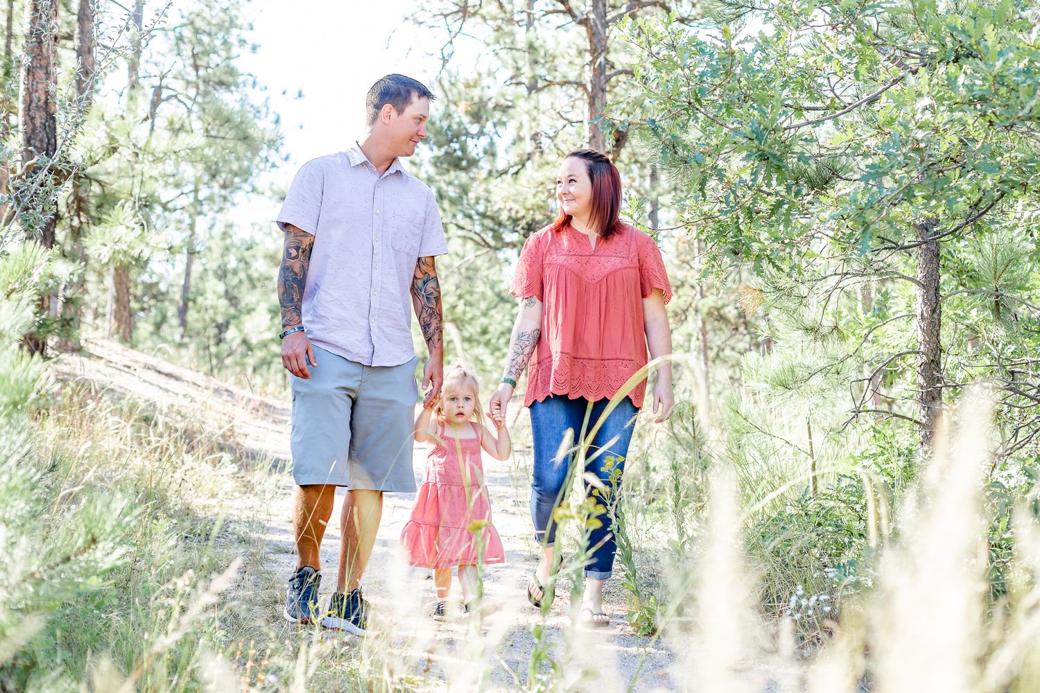 Dad and mom lead their toddler daughter down the trail in Black Forest, Colorado.