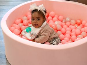Child enjoying playtime in pink ball pit surrounded by colorful balls.