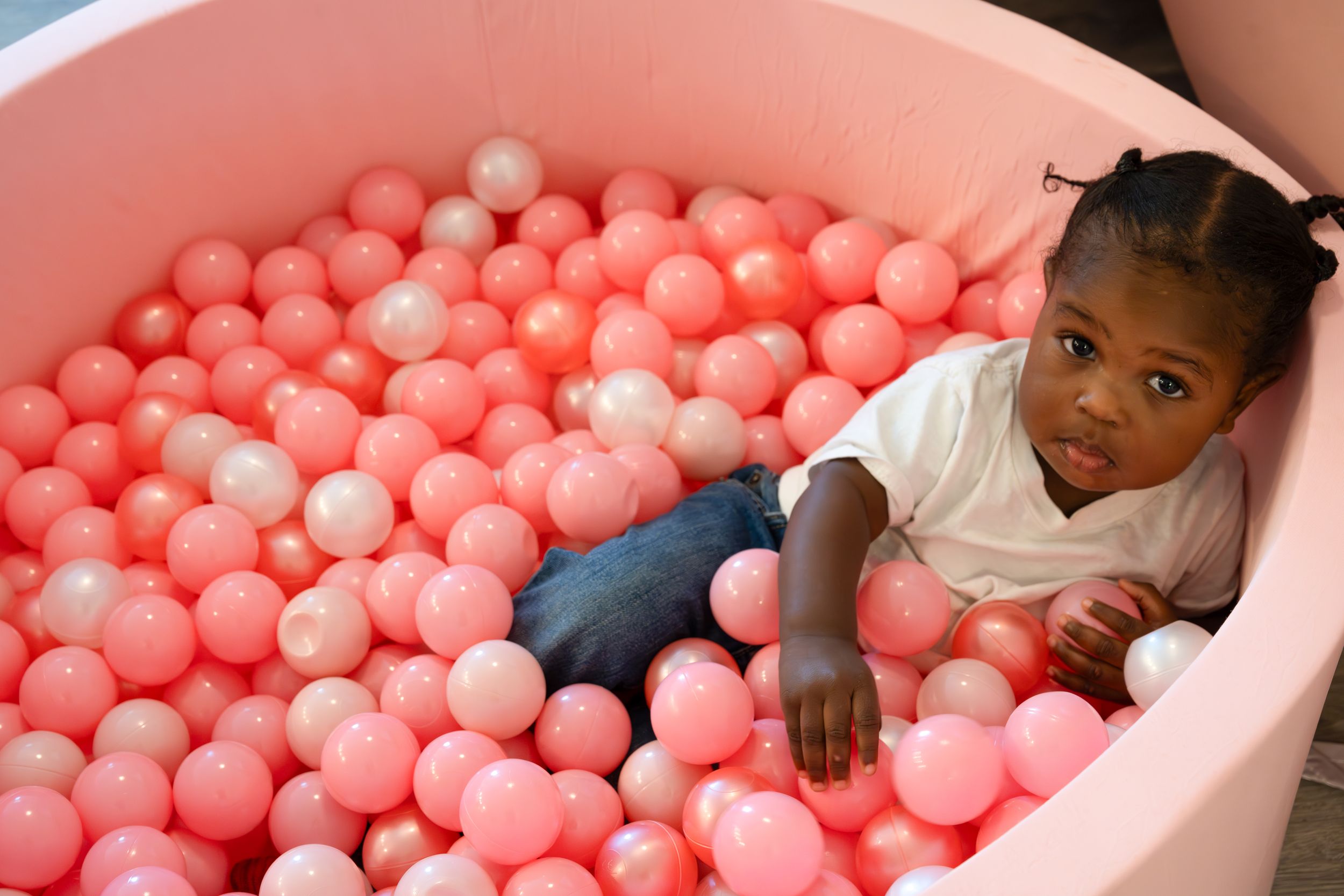 Young child playing in pink ball pit wearing casual clothes.