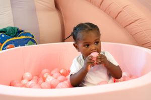 Portrait view of child having fun in pink ball pit with decorative balloons.