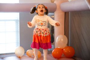Festive party scene with pink ball pit and floating white and orange balloons.